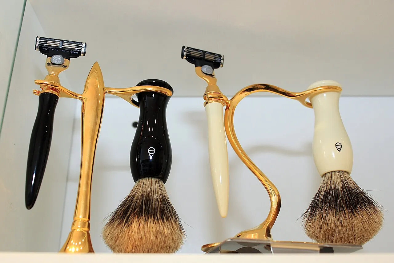 Two sets of modern chrome razor handles and shaving brushes displayed on metallic stands.